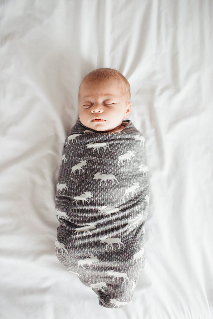 a baby wrapped in a gray swaddle with white moose on it